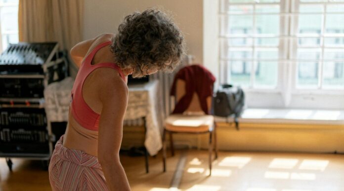 Woman with grey hair stretching in a sunlit room